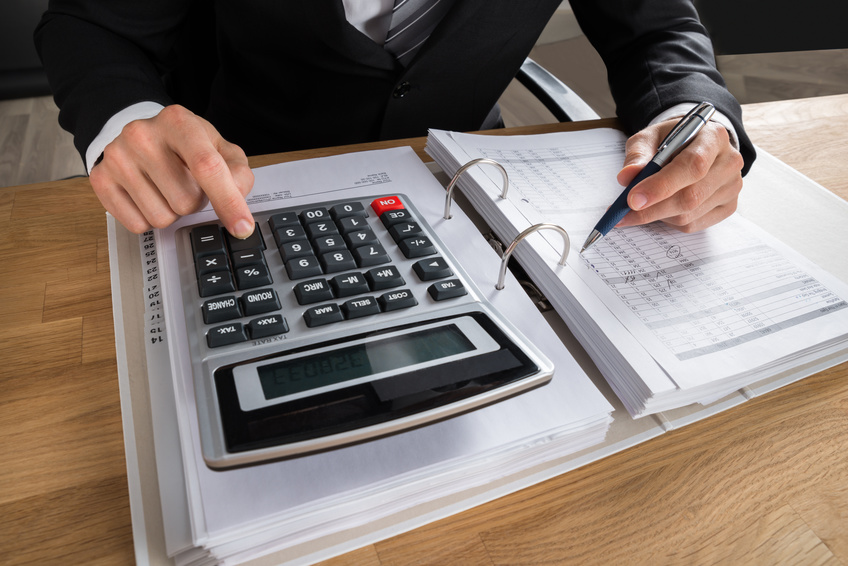 Close-up Of Male Accountant Calculating Tax At Desk In Office